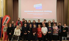 Eine Gruppe von Menschen steht gemeinsam für ein Gruppenfoto im Pankower BVV-Saal. Es handelt die um die Linken Kandidat*innen für die anstehende Wahl zur Bezirksverordnetenversammlung. Viele halten einzelne rote Rosen in den Händen. Im Hintergrund ist auf einer Leinwand das Logo „Die Linke – Bezirksverband Pankow“ sowie der Slogan „Gemeinsam. Solidarisch. Vielfältig.“ zu sehen. Links im Bild steht ein rotes DIE-LINKE-Banner. Die Personen stehen in zwei Reihen und schauen überwiegend in die Kamera.